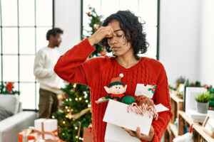 Woman rubs forehead while carrying Christmas decorates as she tries her best to manage holiday stress and anxiety