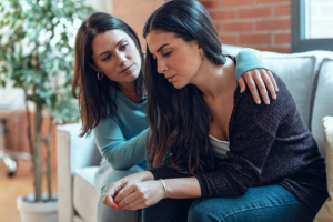 Woman puts arm around friend while learning how to help a loved one with depression