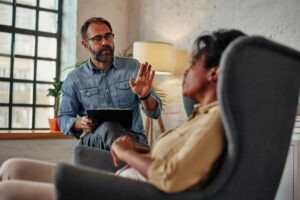 a sitting therapist holds notepad while talking to client in a chair during therapy