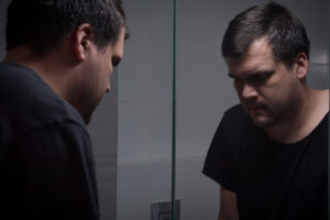 man with low self esteem looks in mirror