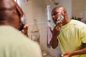 Person thinking about self-care and mental health while shaving in front of a mirror