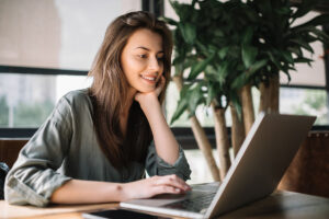 smiling woman sits at desk on laptop searching for mental health providers
