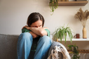 upset woman sits on her couch curled up enduring anxiety symptoms in women