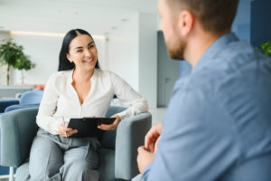 smiling woman with a notepad talks to patient in therapy about psychiatric care